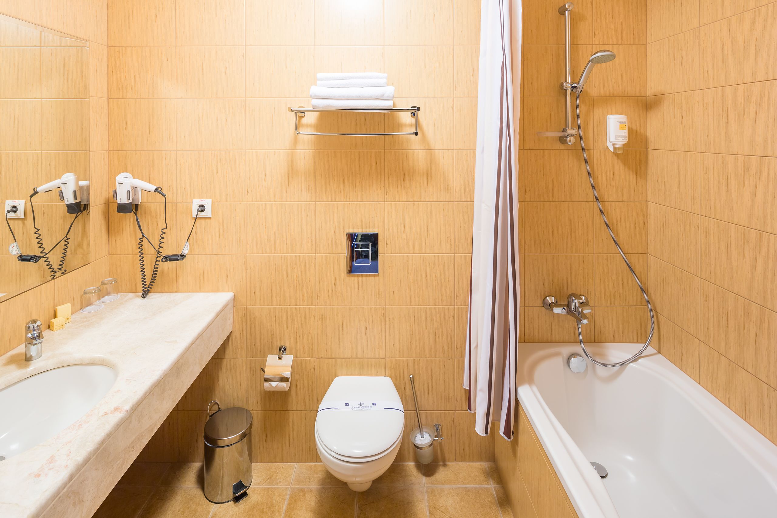 Un baño con lavamanos, inodoro y bañera. Hay toallas en un estante y se ve una cortina de ducha.