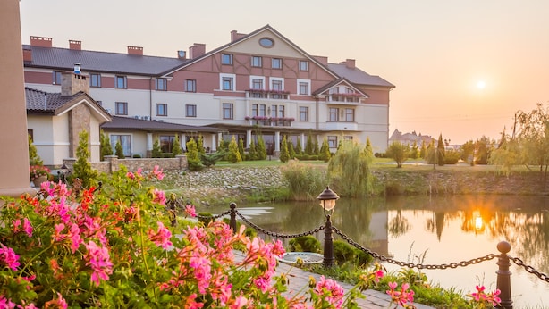 A hotel with a large building, a pond, and pink flowers in the foreground. - Panska Gora (Lviv)