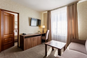 A hotel room with a bed, a desk with a telephone, a flat-screen TV, a lamp, a chair, a sofa, and a window with curtains. - Panska Gora (Lviv)