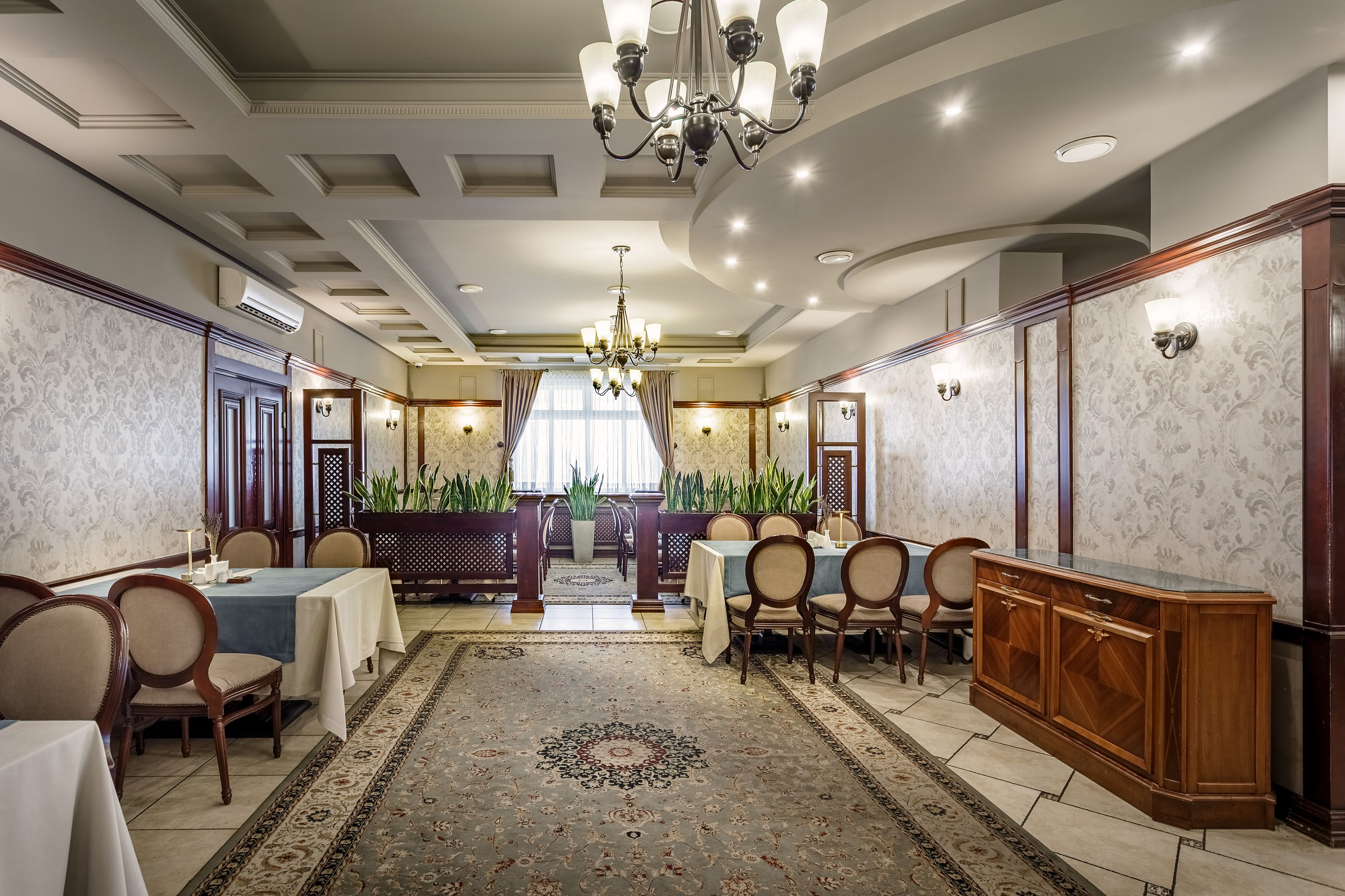 A formal dining room with a chandelier, patterned wallpaper, and a central table with chairs.