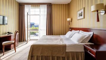 A hotel room with a bed, a desk, a chair, a television, and a window with curtains.