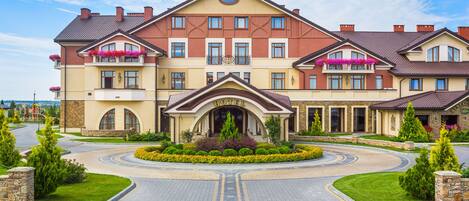 A large hotel with a central entrance, multiple balconies with flower boxes, and a landscaped driveway.
