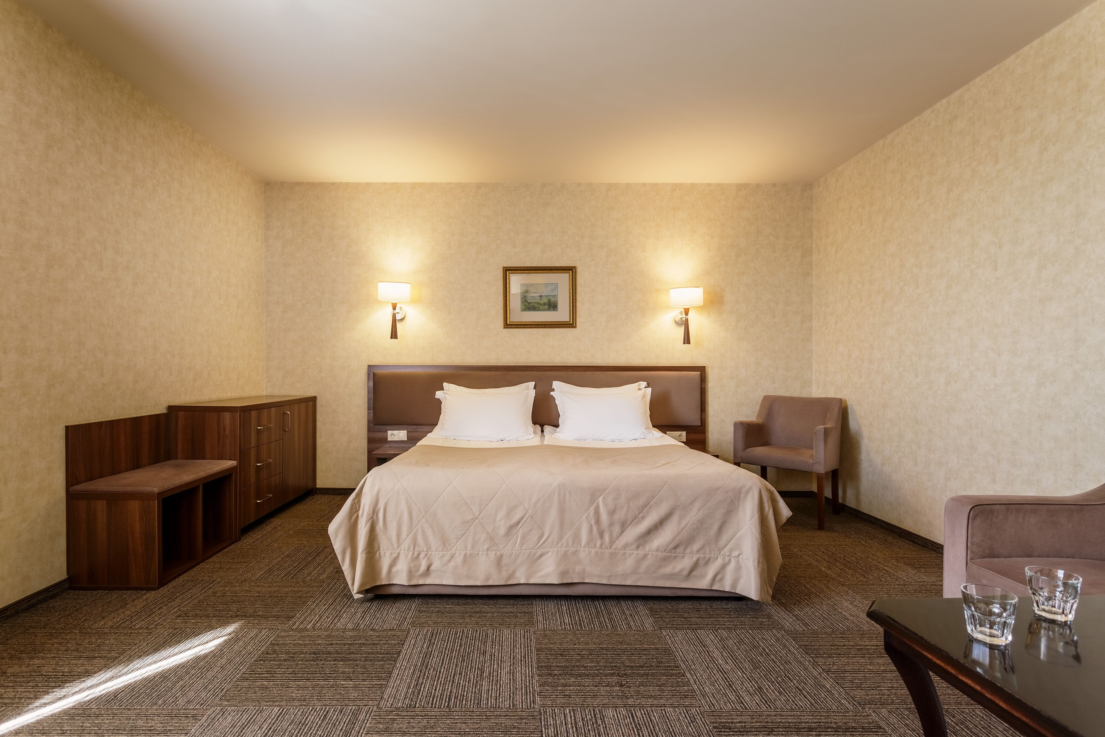 Habitación de hotel con cama, mesitas de noche, escritorio, silla y un cuadro en la pared.