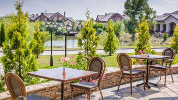 An outdoor patio with a table and chairs, a stone wall, and a view of houses and a body of water.