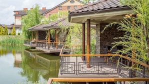 A riverside restaurant with outdoor seating, stone pillars, and a view of residential buildings. - Panska Gora (Lviv)