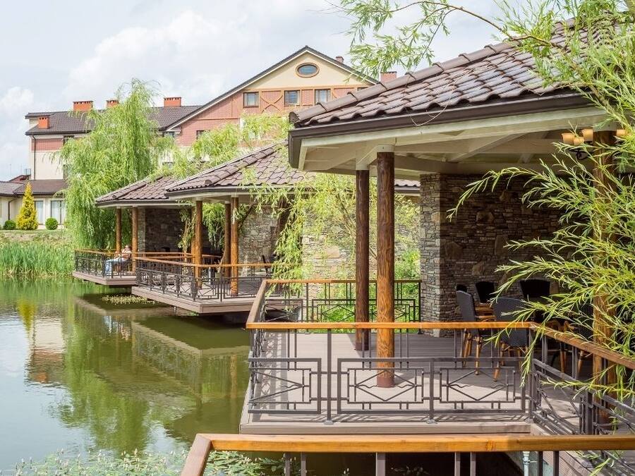 Un restaurante a orillas del río con terraza, pilares de piedra y vistas a edificios residenciales.