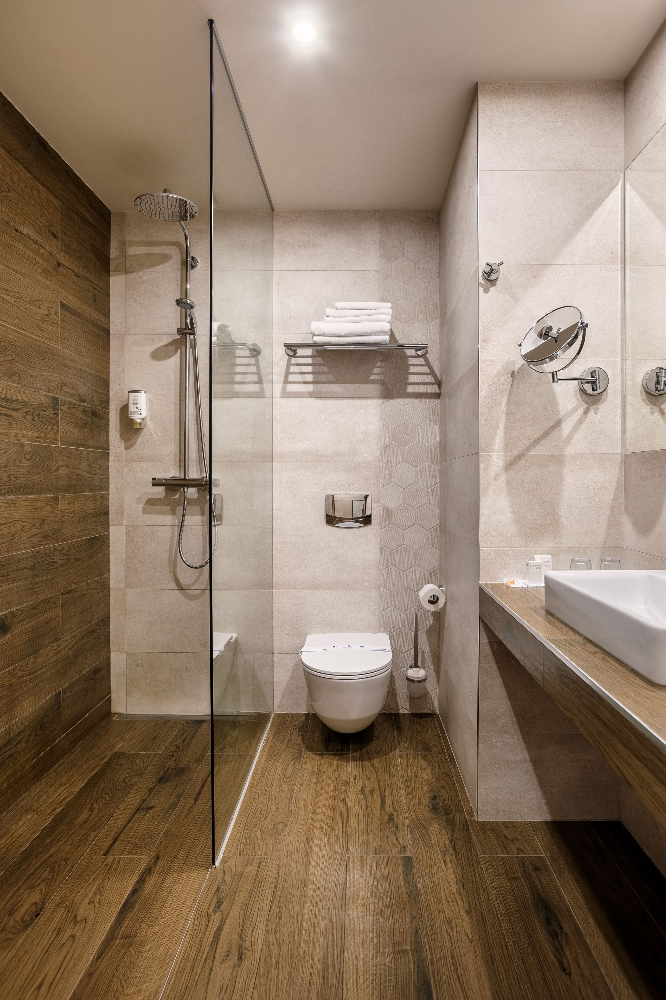 Une salle de bain moderne avec une douche à parois de verre, un plancher en bois, des toilettes et un lavabo avec un miroir.