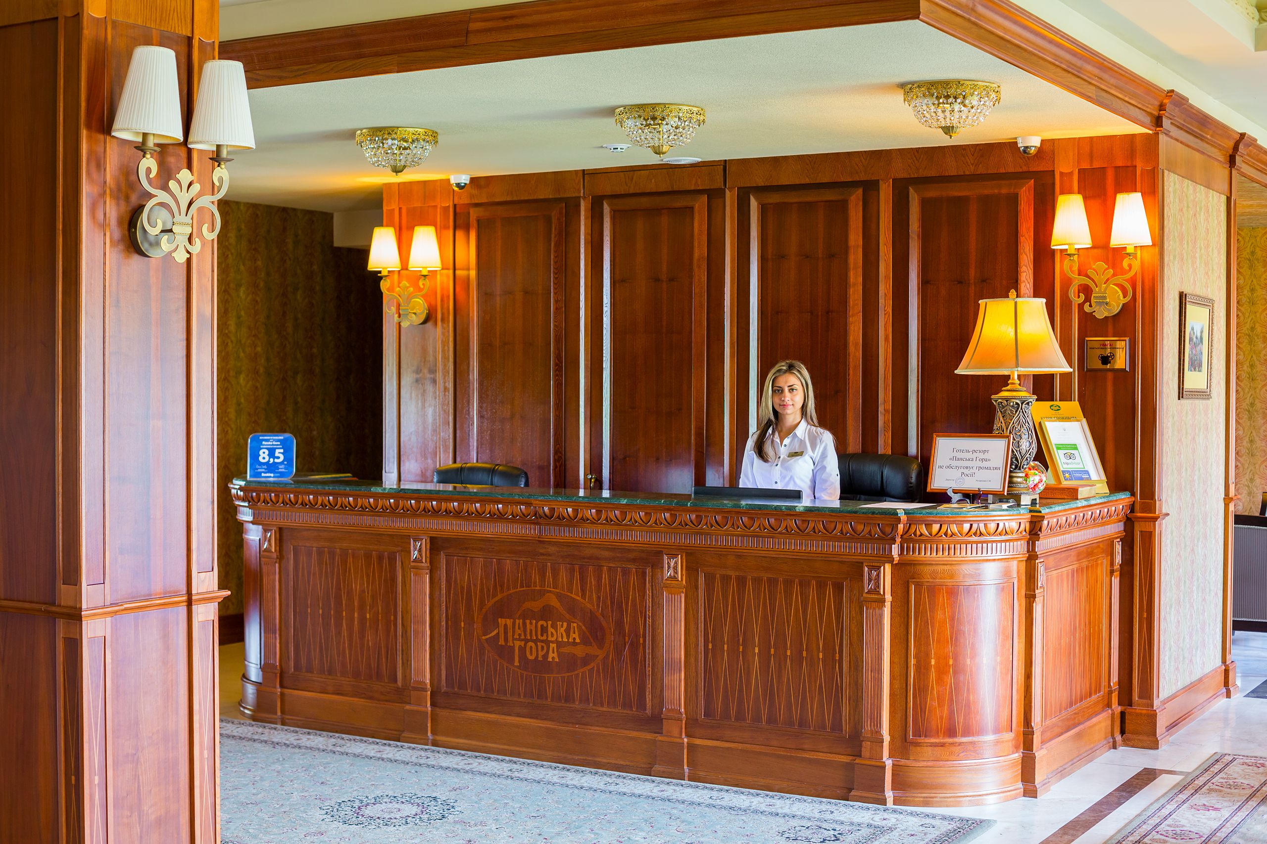 Un mostrador de recepción de madera con una recepcionista, una araña de cristal y un cartel de bienvenida enmarcado.