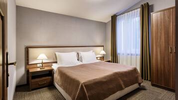 A hotel room with a large bed, two bedside tables with lamps, a wardrobe, and a window with curtains.