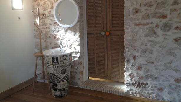 Un baño con una puerta de madera, un espejo redondo y un lavabo con una pila estampada.