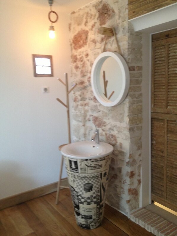 Un baño con un diseño de lavamanos original, un espejo y un perchero de madera.