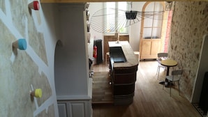 Una escalera que conduce a un suelo de madera, una zona de cocina con un lavamanos y armarios, y un comedor con sillas y una mesa.