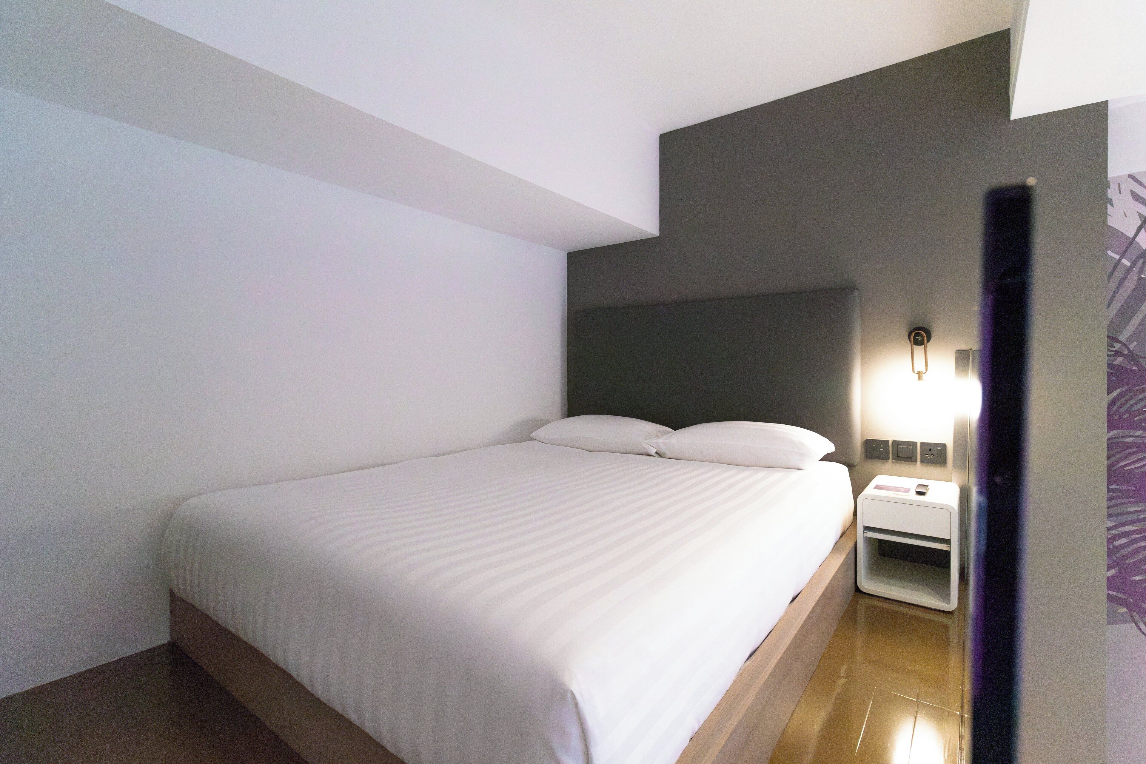 Una habitación de hotel moderna con una cama grande, una mesita de noche y una lámpara.