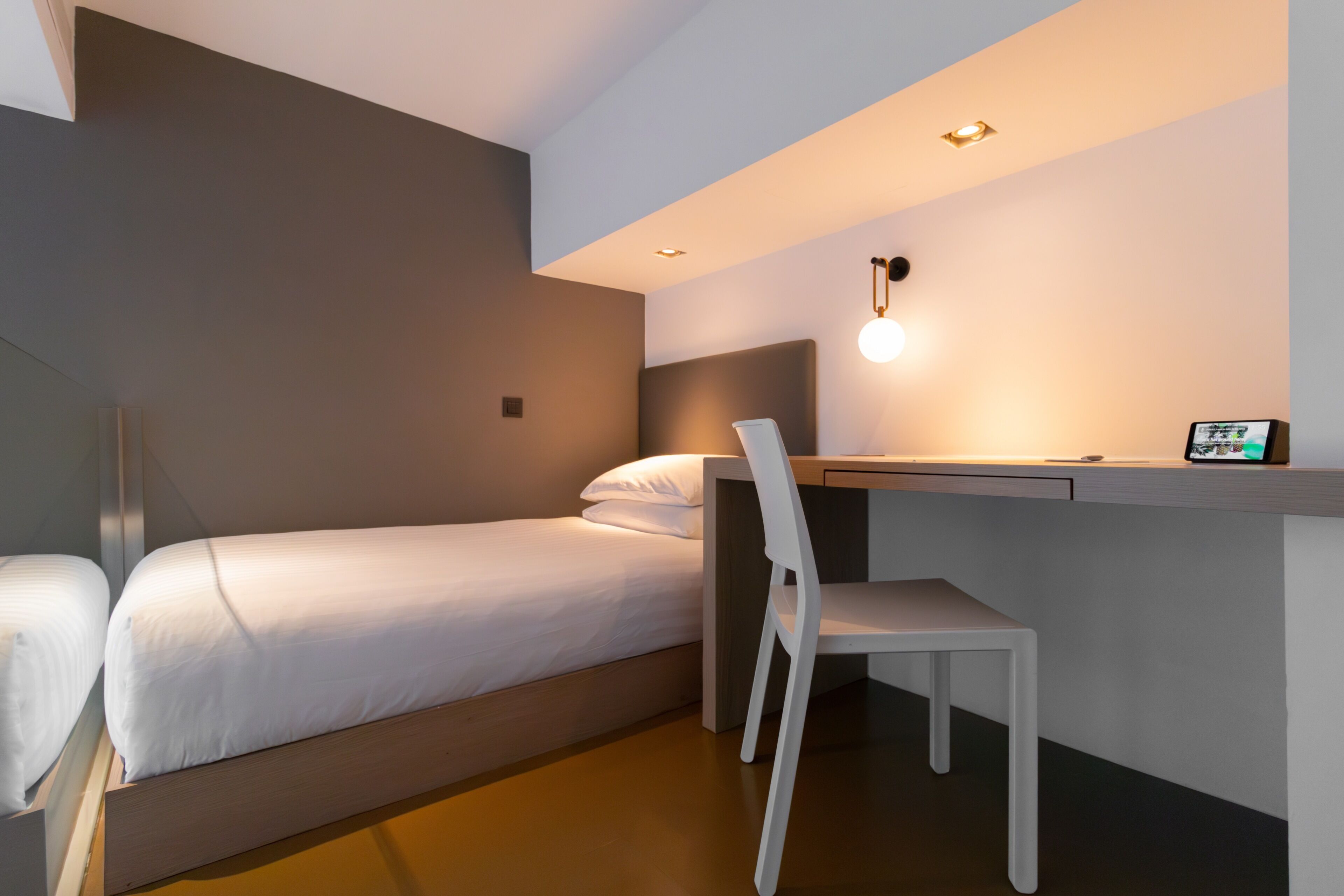 A compact hotel room with a single bed, a desk, and a chair.