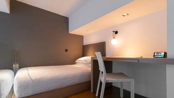 A compact hotel room with a single bed, a desk, and a chair.