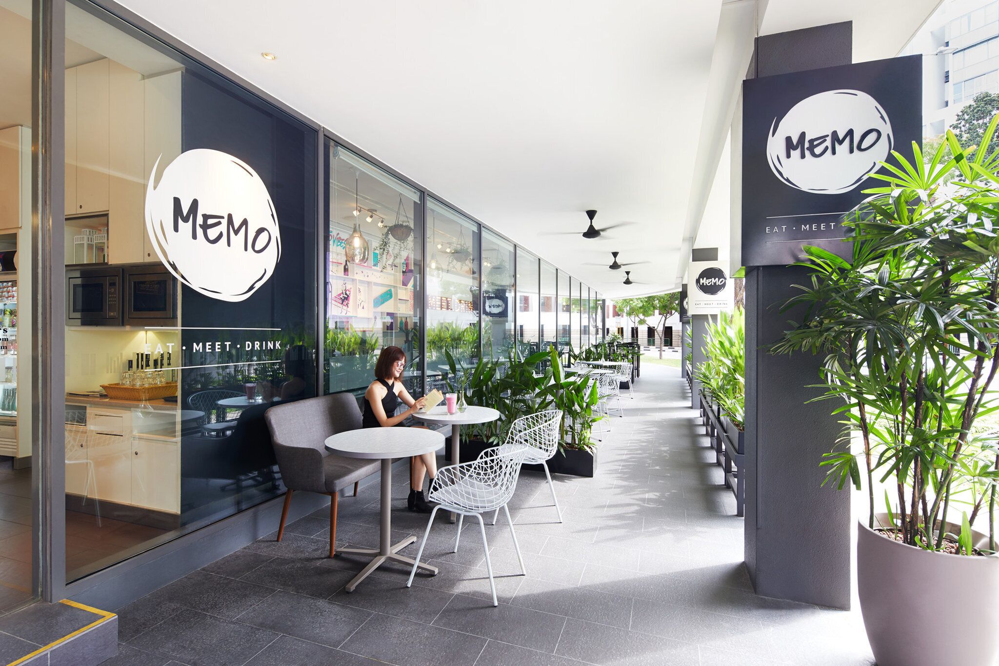 Una cafetería de diseño moderno, con paredes de vidrio, sillas blancas y plantas de interior.
