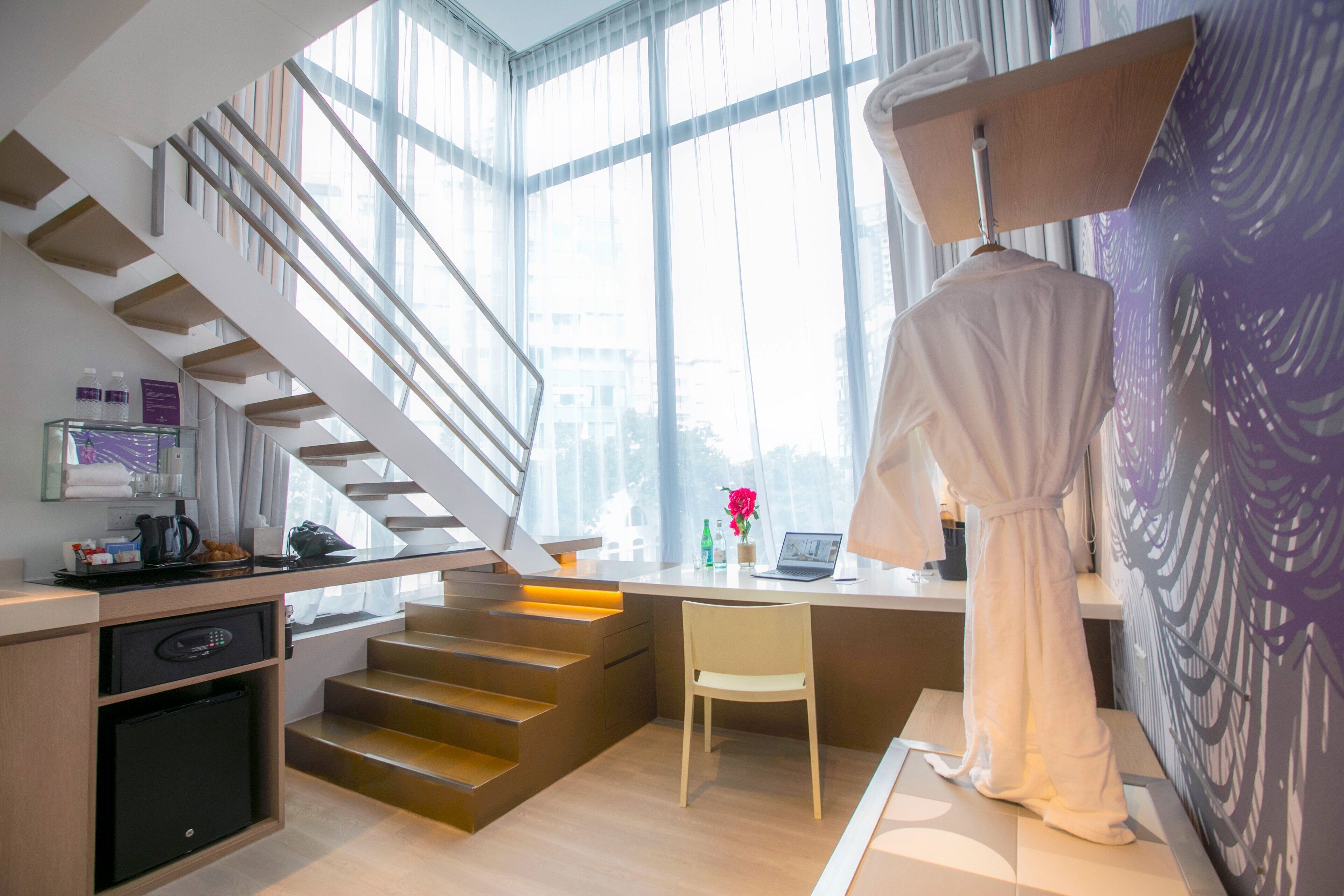 Ein modernes Hotelzimmer mit Treppe, Schreibtisch, Stuhl und einem an der Wand hängenden Bademantel.