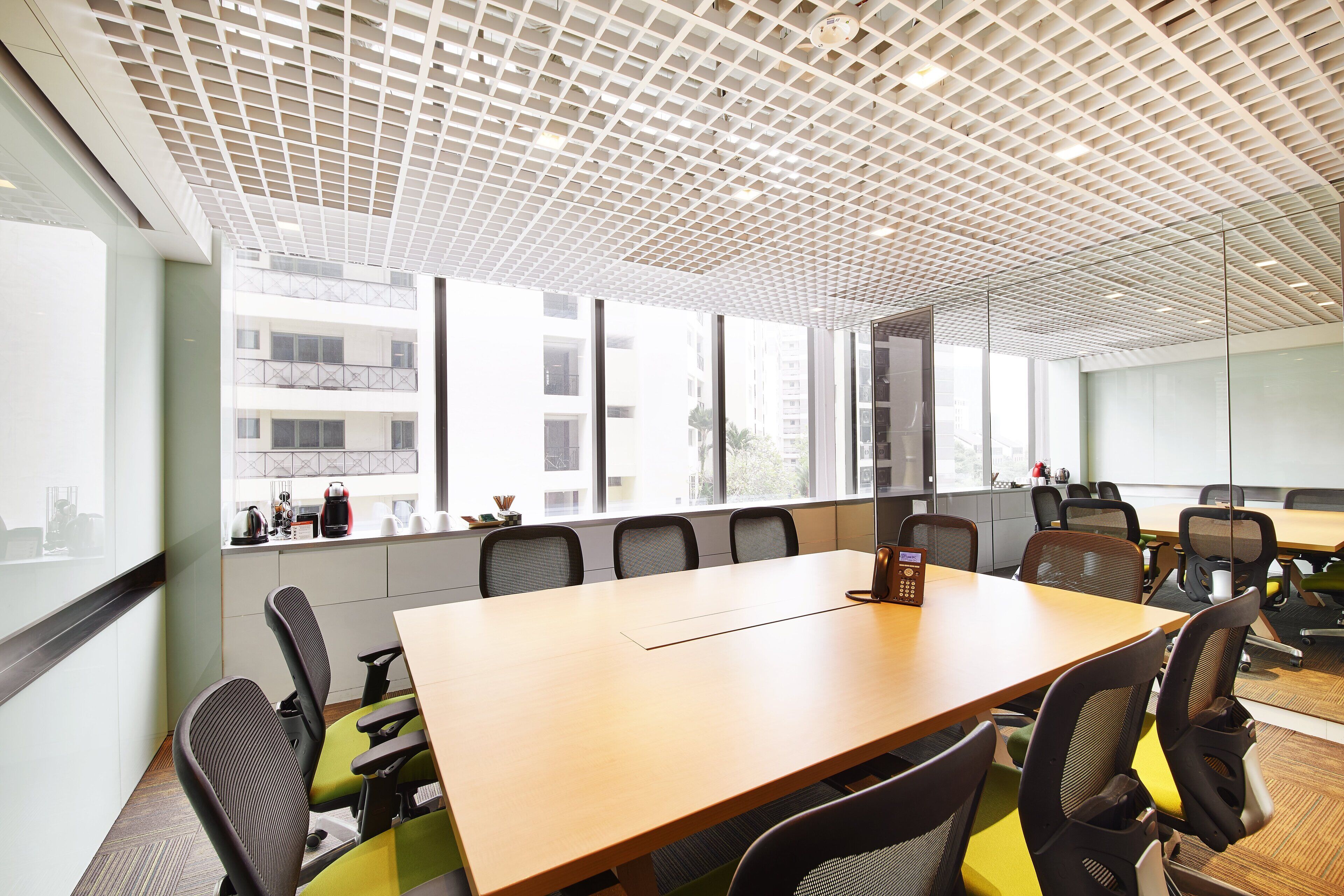 Un salón de conferencias con una larga mesa, numerosas sillas y grandes ventanales con vistas a edificios.
