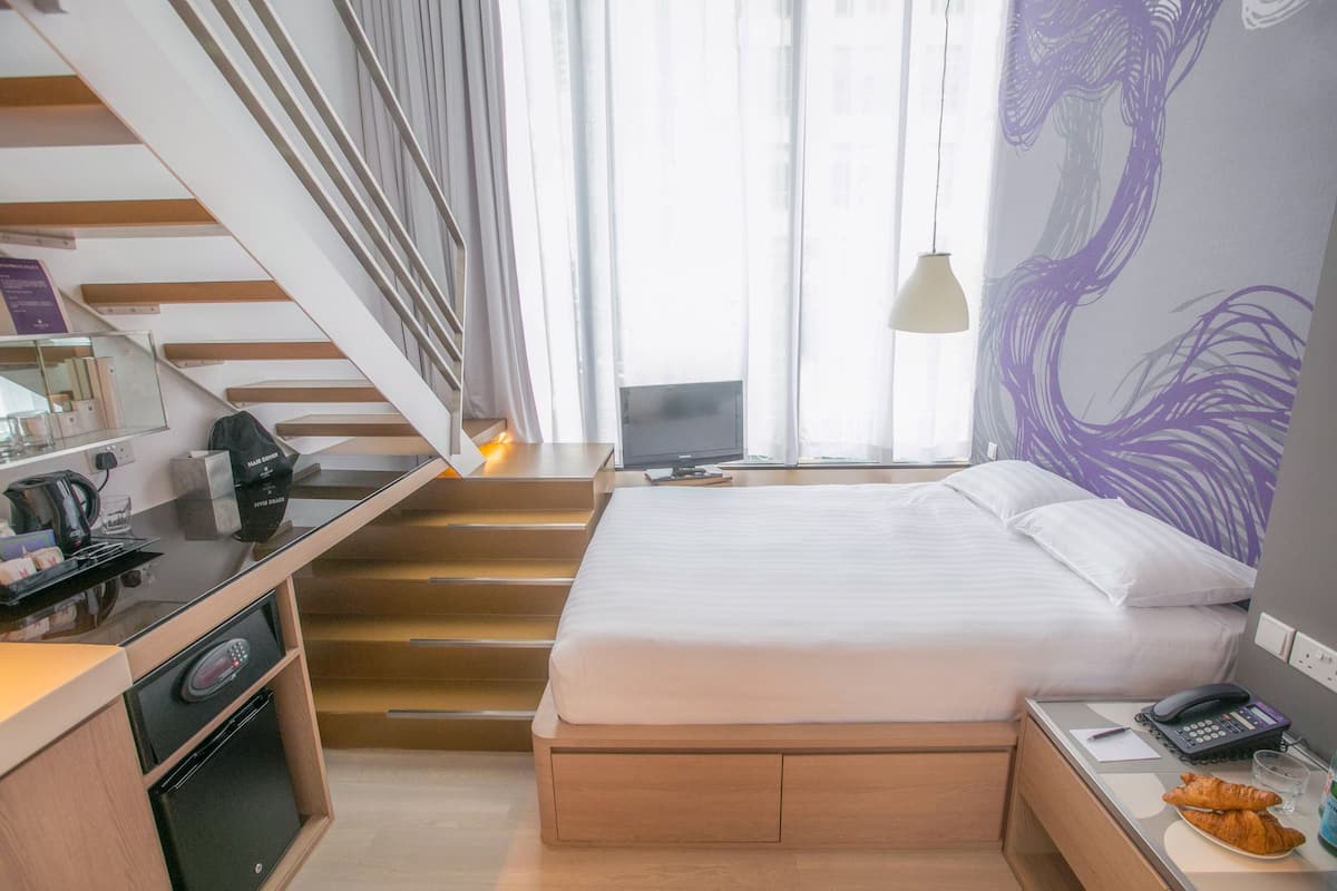 A hotel room with a bed, a desk, a coffee machine, a TV, and a staircase.