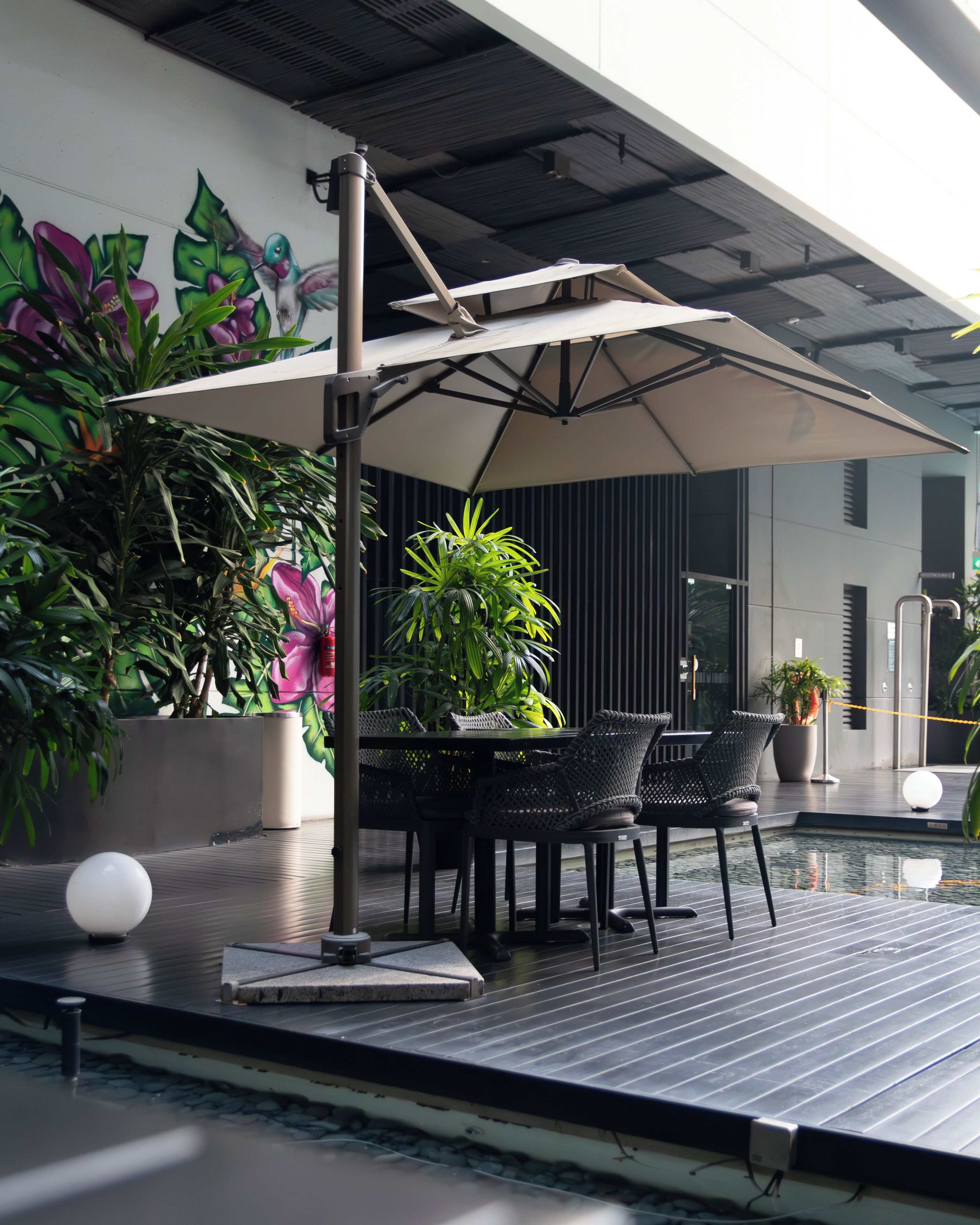 An outdoor patio with a table and chairs, surrounded by potted plants and a mural.