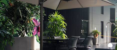 An outdoor patio with a table and chairs, surrounded by potted plants and a mural.