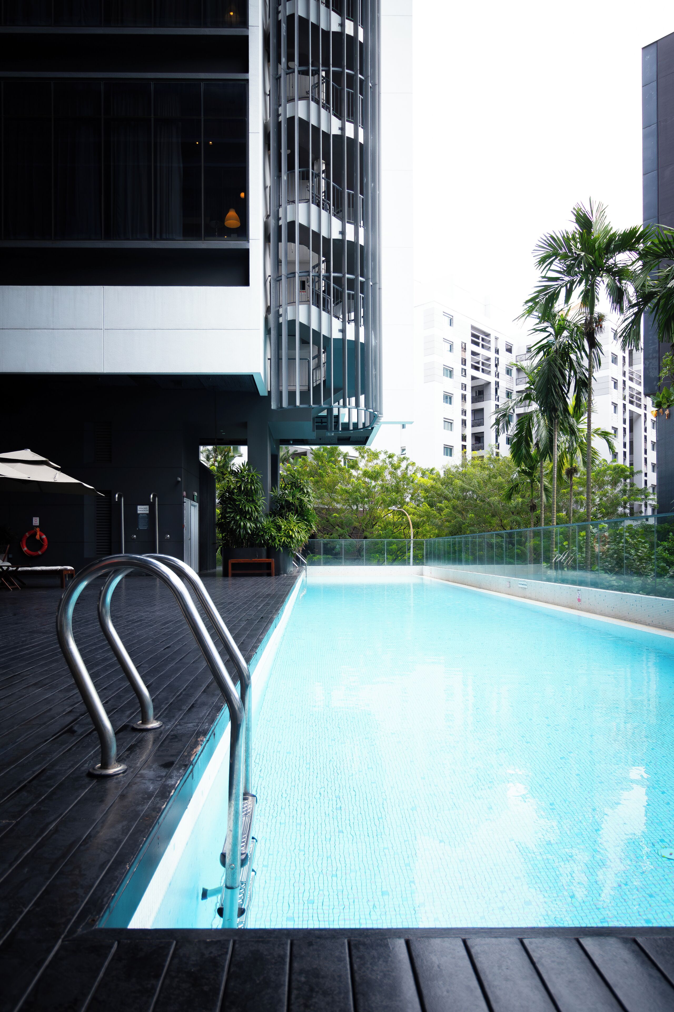 Una piscina con una escalera de metal, rodeada por una terraza de madera y una barandilla de metal.
