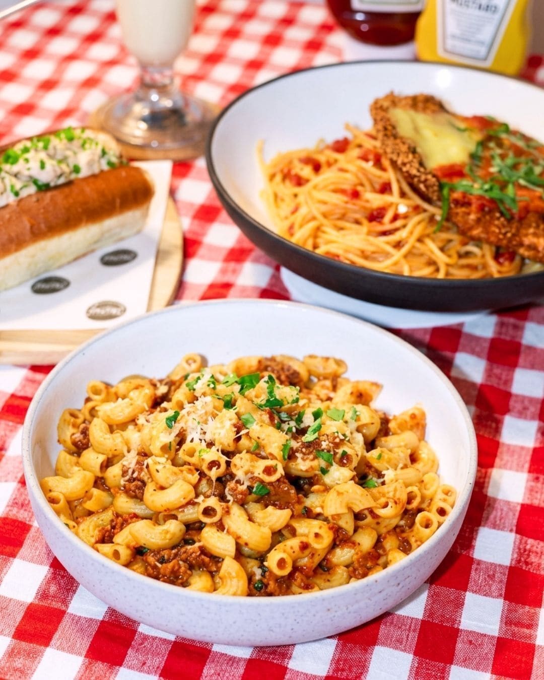 A dining table with a checkered tablecloth, a bowl of pasta, and a plate of spaghetti.