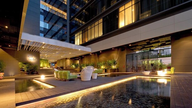 A modern hotel lobby with a central pool, seating areas, and a view of the building's exterior. - Studio M Hotel Singapore (Singapore)