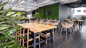 An indoor dining area with wooden tables and wicker chairs, a green wall, and ceiling fans. - Studio M Hotel Singapore (Singapore)