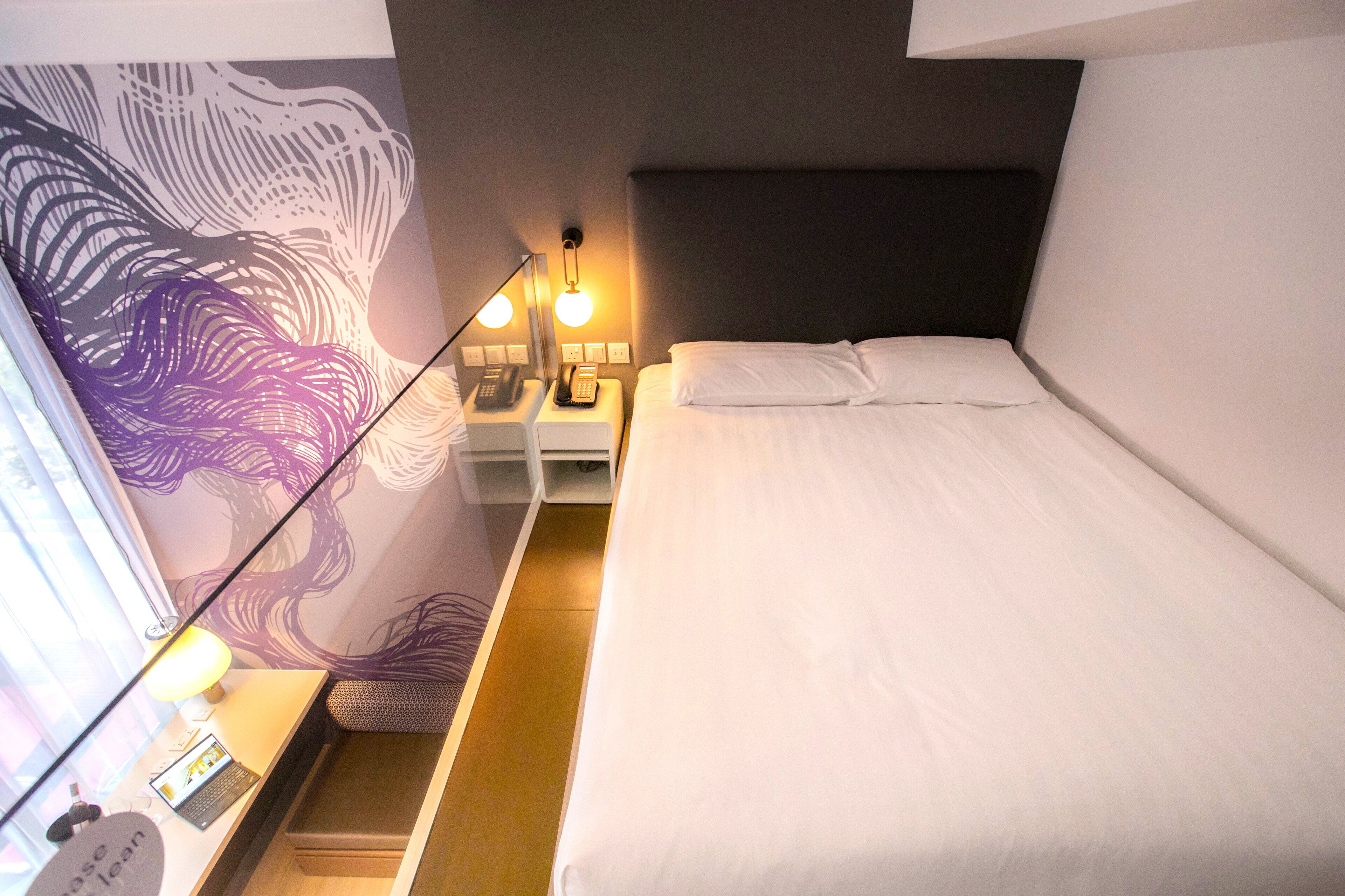 A hotel room with a bed, bedside table, lamp, and a wall with a decorative design.