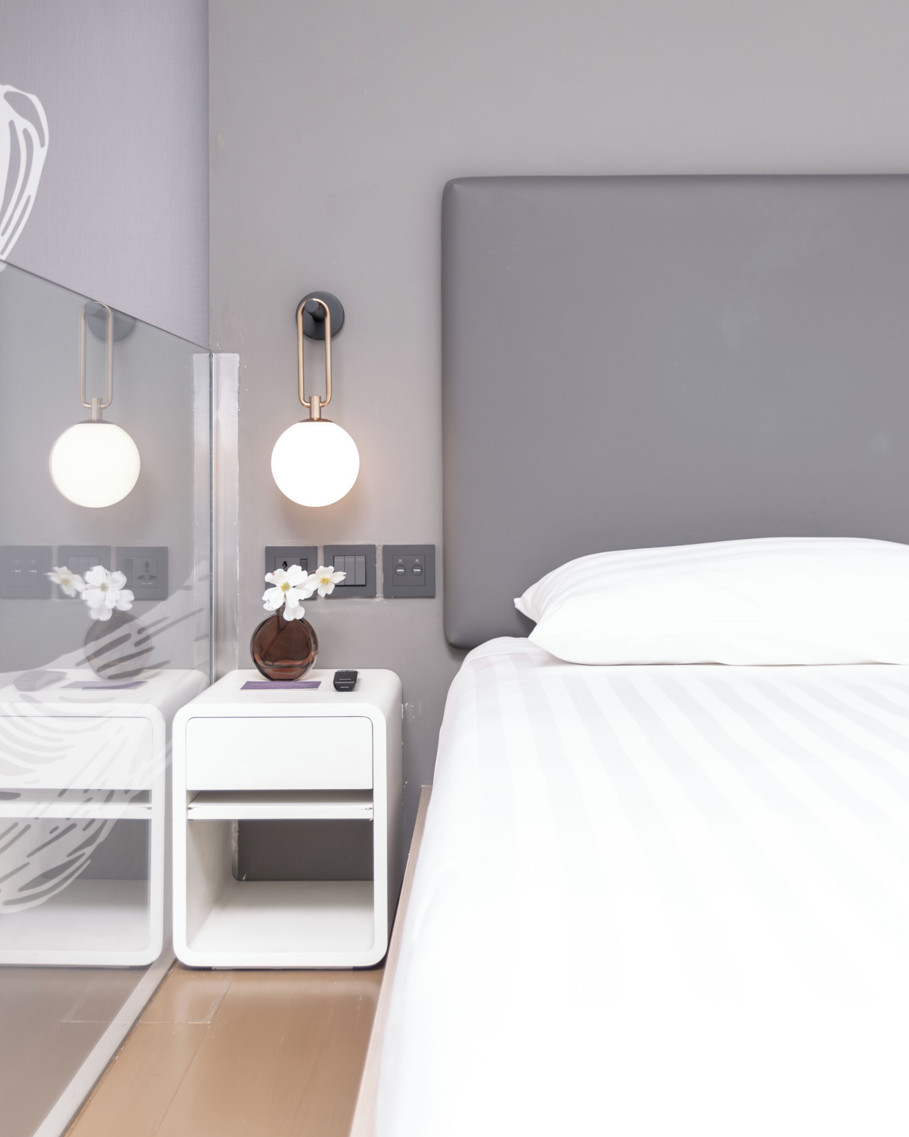 Un hotel moderno con una cama grande, una mesita de noche con un florero y una lámpara de pared.