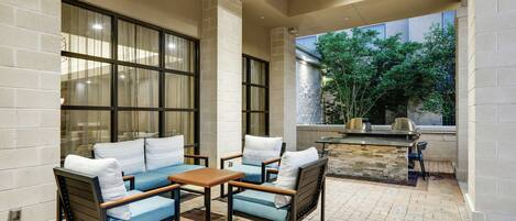 An outdoor patio with a brick floor, two sofas with cushions, a wooden table, and a stone fireplace.