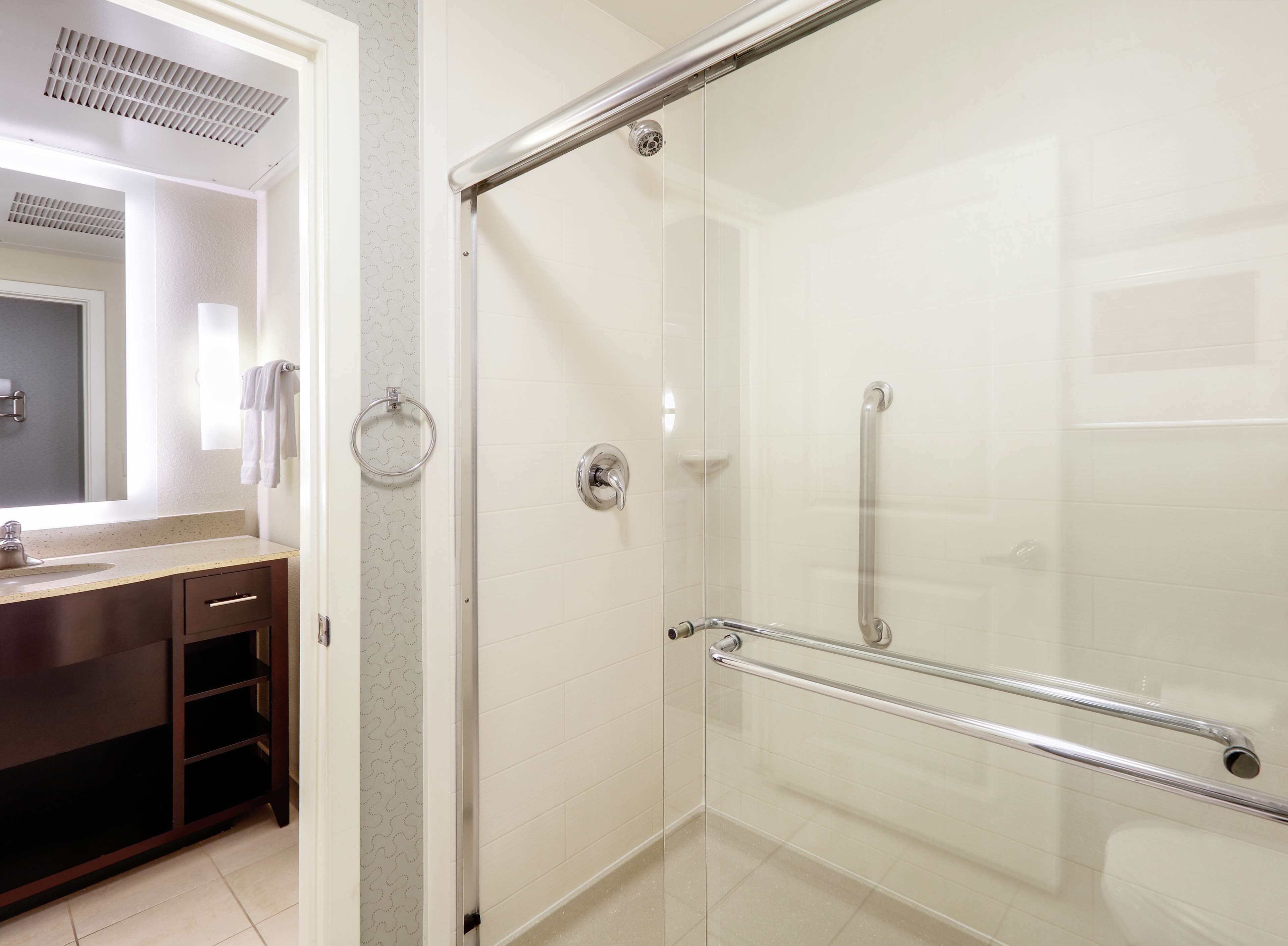 Un baño moderno con cabina de ducha de vidrio, tocador con detalles en madera oscura y un salpicadero decorativo.