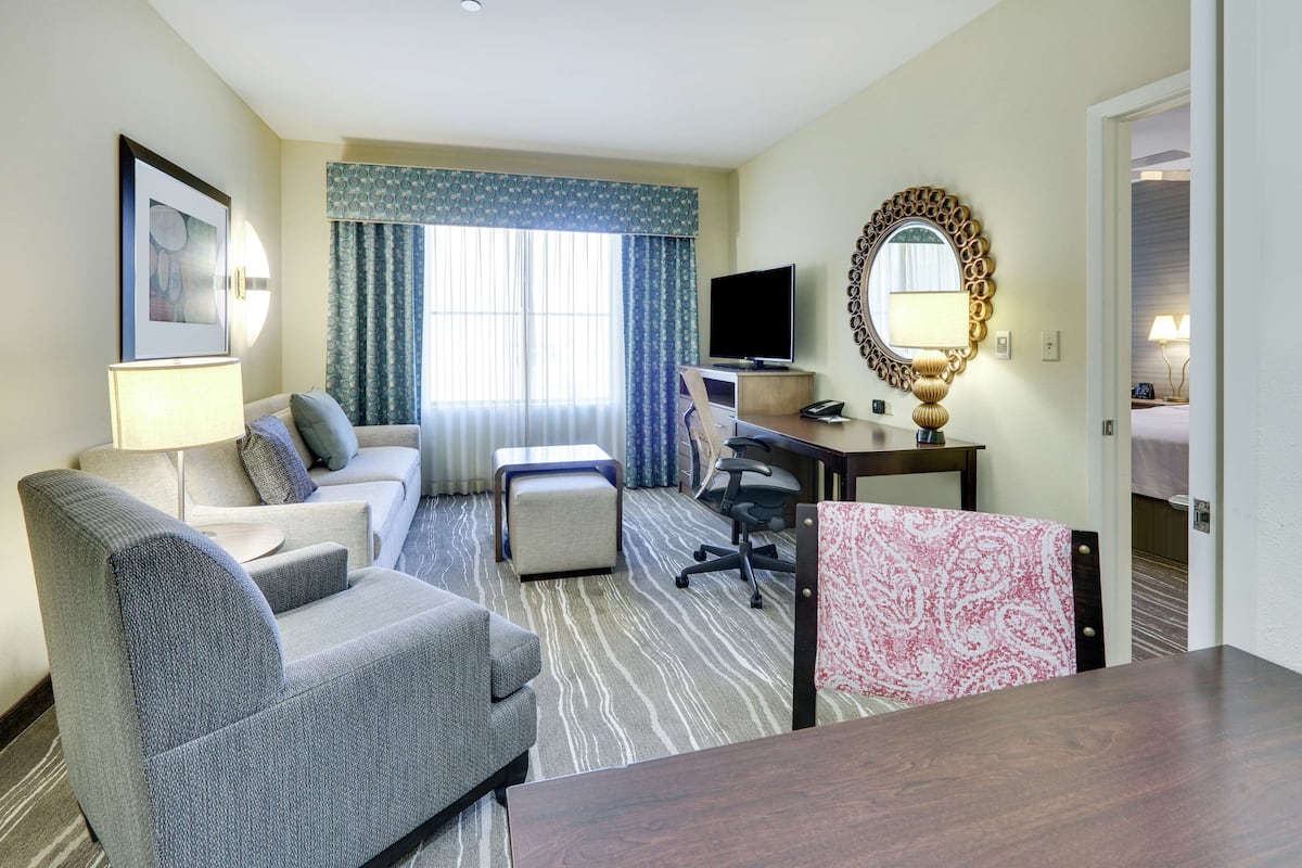 Une chambre d’hôtel équipée d’un canapé, d’un fauteuil, d’un bureau, d’une télévision et d’un miroir.