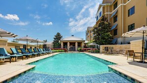 A swimming pool with lounge chairs and umbrellas, surrounded by a building with multiple floors and a covered area. - Homewood Suites Dallas Allen (Allen)