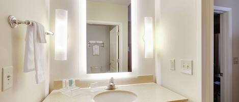 A bathroom with a sink, mirror, towel rack, and a door leading to another room.