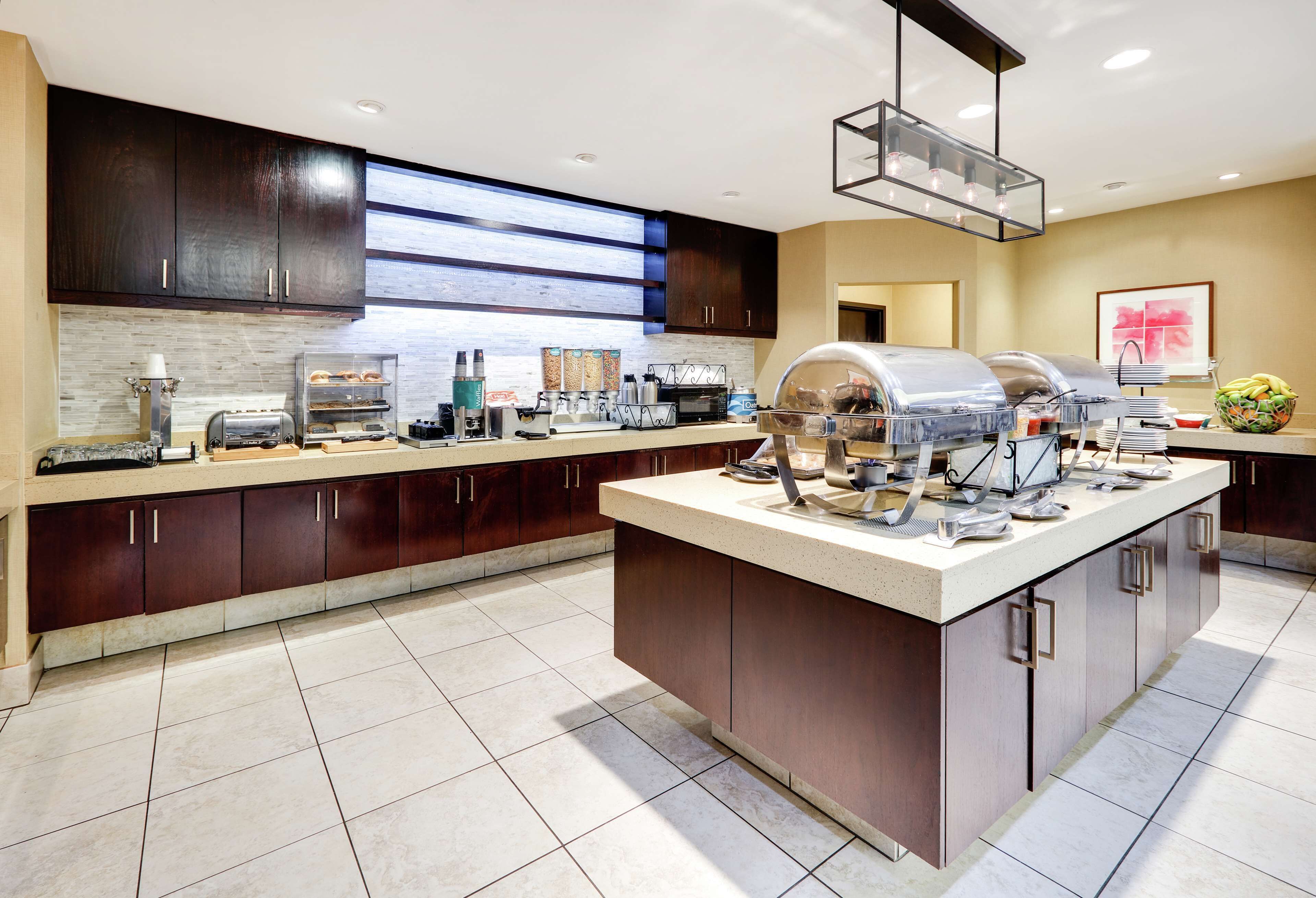 A modern kitchen with dark wood cabinets, a large island with a grill, and a breakfast bar.