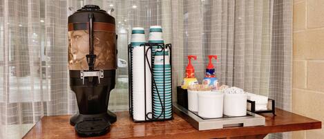 A coffee machine, stacked cups, and condiment bottles on a wooden table.