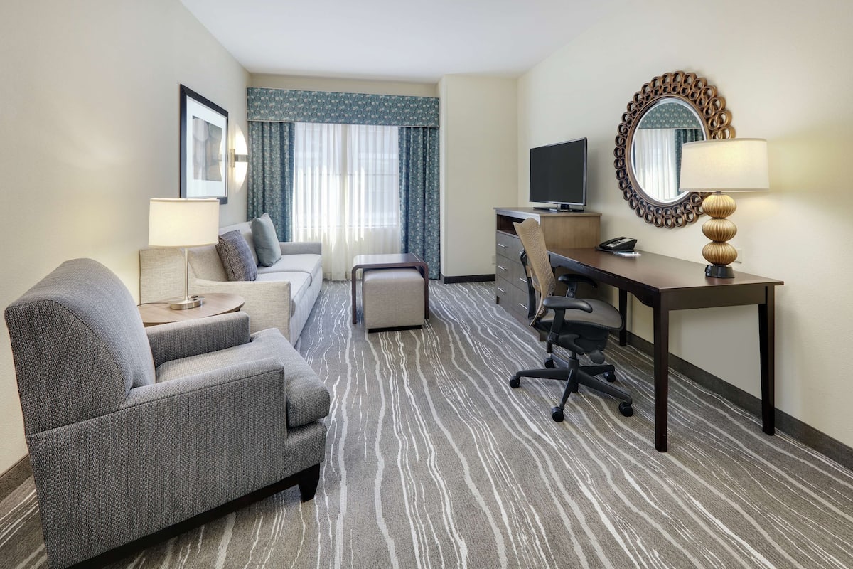 Une chambre d’hôtel équipée d’un canapé, d’un bureau avec une chaise, d’une télévision, d’une lampe et d’un grand miroir.