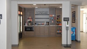 A Candlewood Cupboard with a microwave, coffee machine, and various products on shelves.