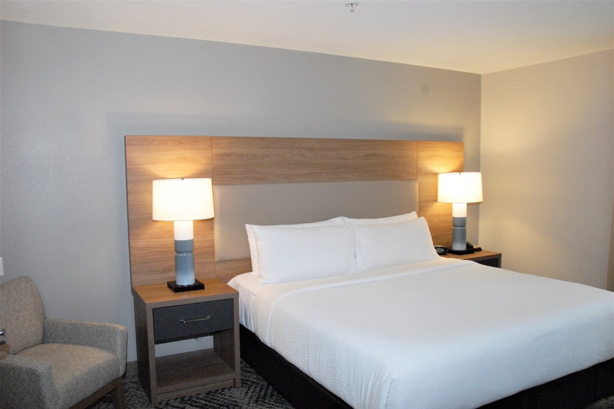 Een hotelkamer met een groot bed, twee nachtkastjes met lampen, een stoel en een houten hoofdbord.
