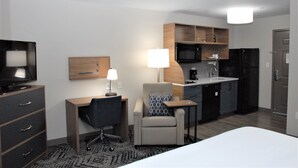 A hotel room with a bed, a desk with a chair, a television, a microwave, a refrigerator, and a small kitchenette.