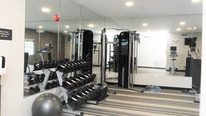 A gym with exercise equipment, a mirrored wall, and a carpeted floor.