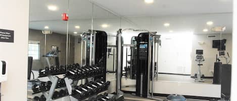 A gym with exercise equipment, a mirrored wall, and a carpeted floor.