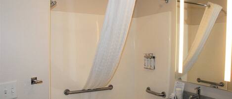 A bathroom with a shower, grab bars, a sink, and a mirror.