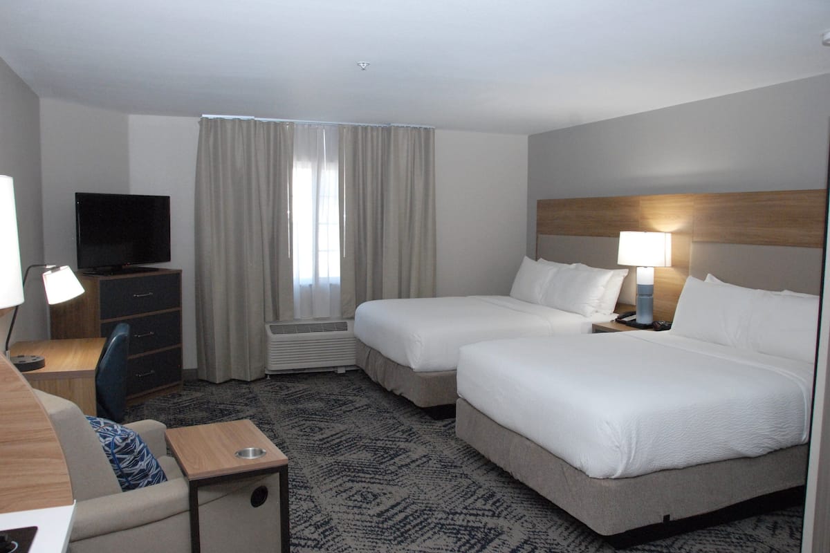Een hotelkamer met twee bedden, een bureau met een televisie, een lamp en een raam met gordijnen.