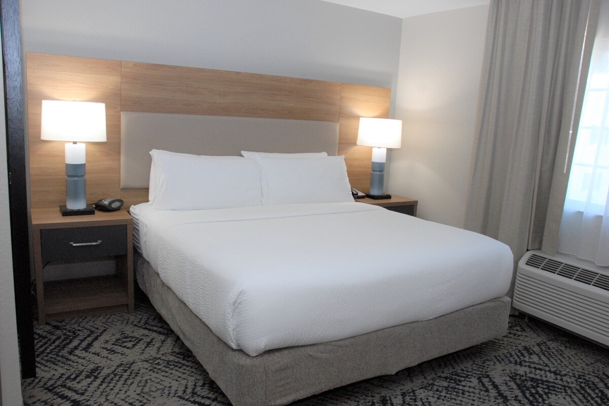 A neatly made bed with white linens, two bedside lamps, a nightstand with a drawer, and a patterned carpet.