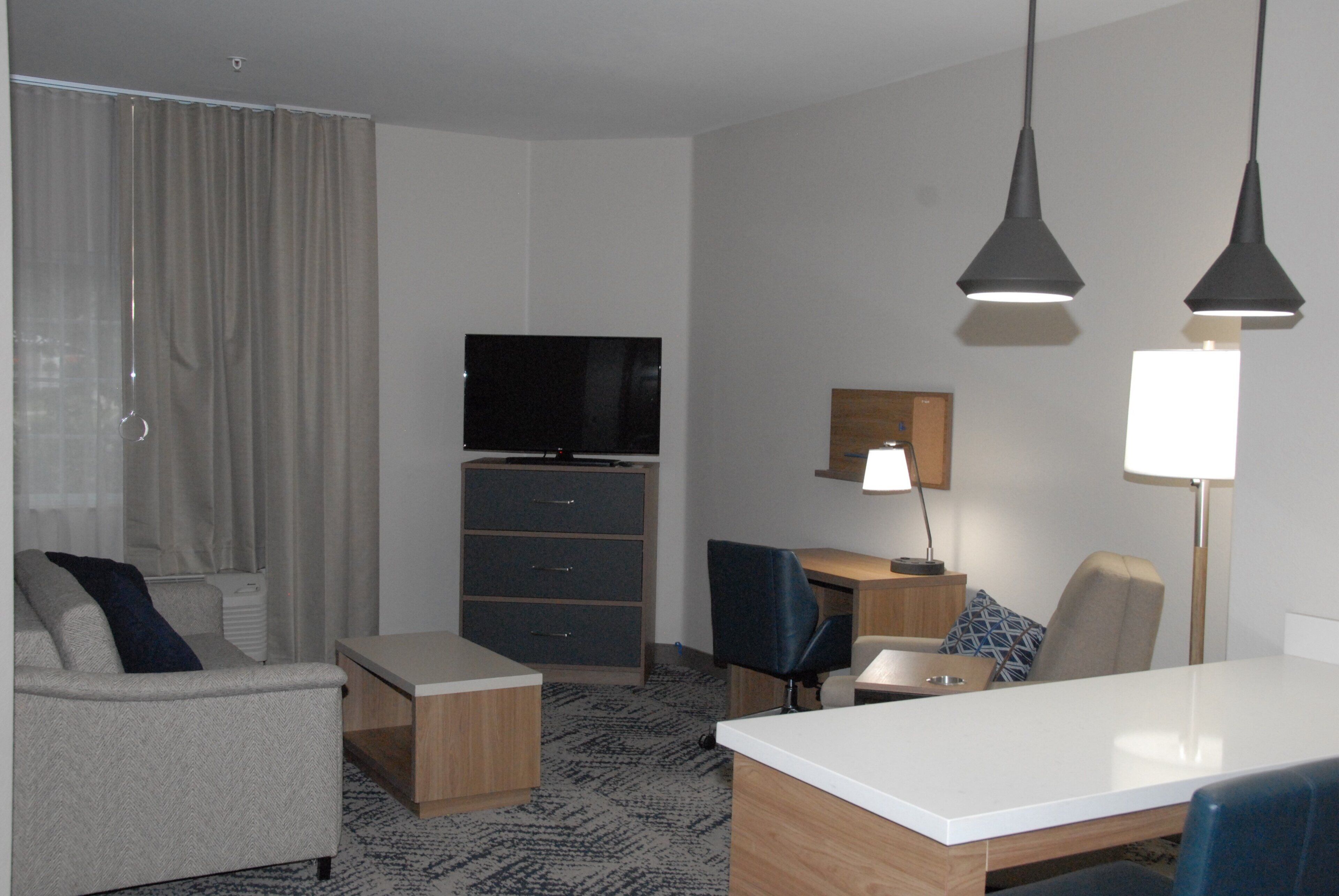 A hotel room with a sofa, a desk, a television, a lamp, and a patterned carpet.
