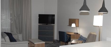 A hotel room with a sofa, a desk, a television, a lamp, and a patterned carpet.