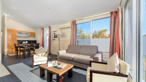 A modern living room with a sofa, chairs, a coffee table, and a dining area with a kitchen in the background. - Appart’Hôtel La Villa Carnot Cannes (Cannes)